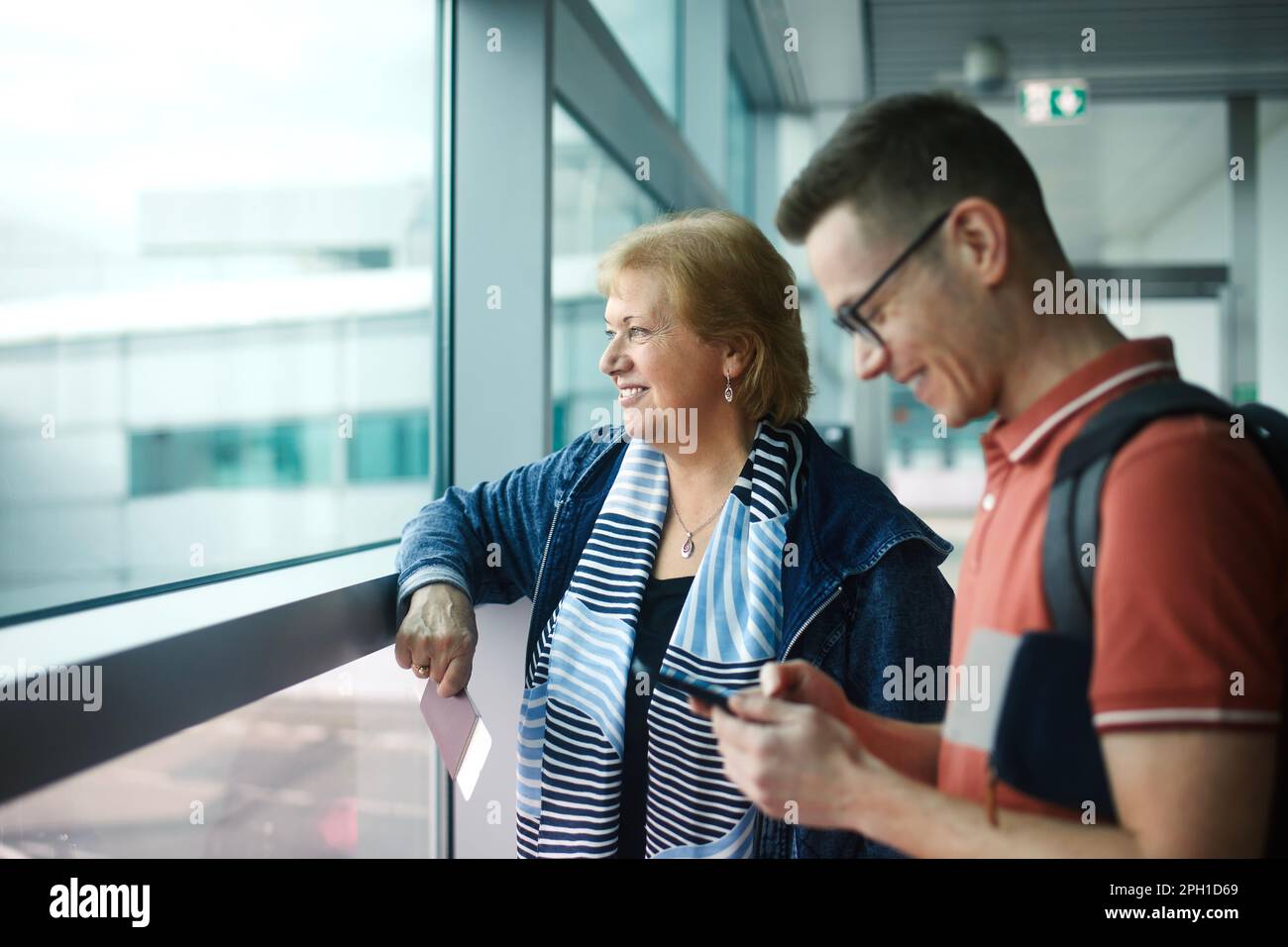 Passagiere warten am Flughafen. Glückliche Seniorin mit ihrem erwachsenen Sohn vor dem Einsteigen in das Flugzeug. Stockfoto