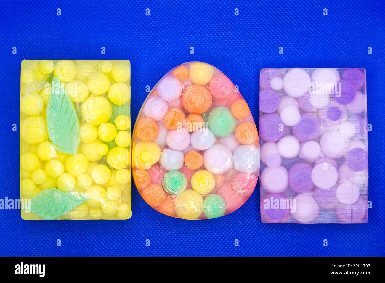 Drei durchsichtige Seifenstücke mit bunten Kugeln auf blauem Hintergrund. Stockfoto