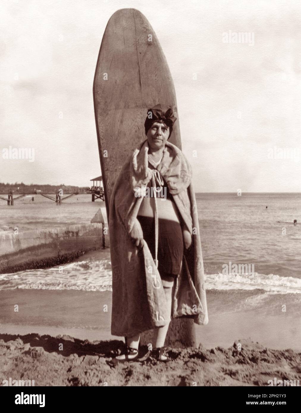 Vintage-Porträt einer Seniorin in den 1920er Jahren, die mit einem hölzernen Surfbrett am Waikiki Beach in Honolulu, Hawaii, posiert. Stockfoto