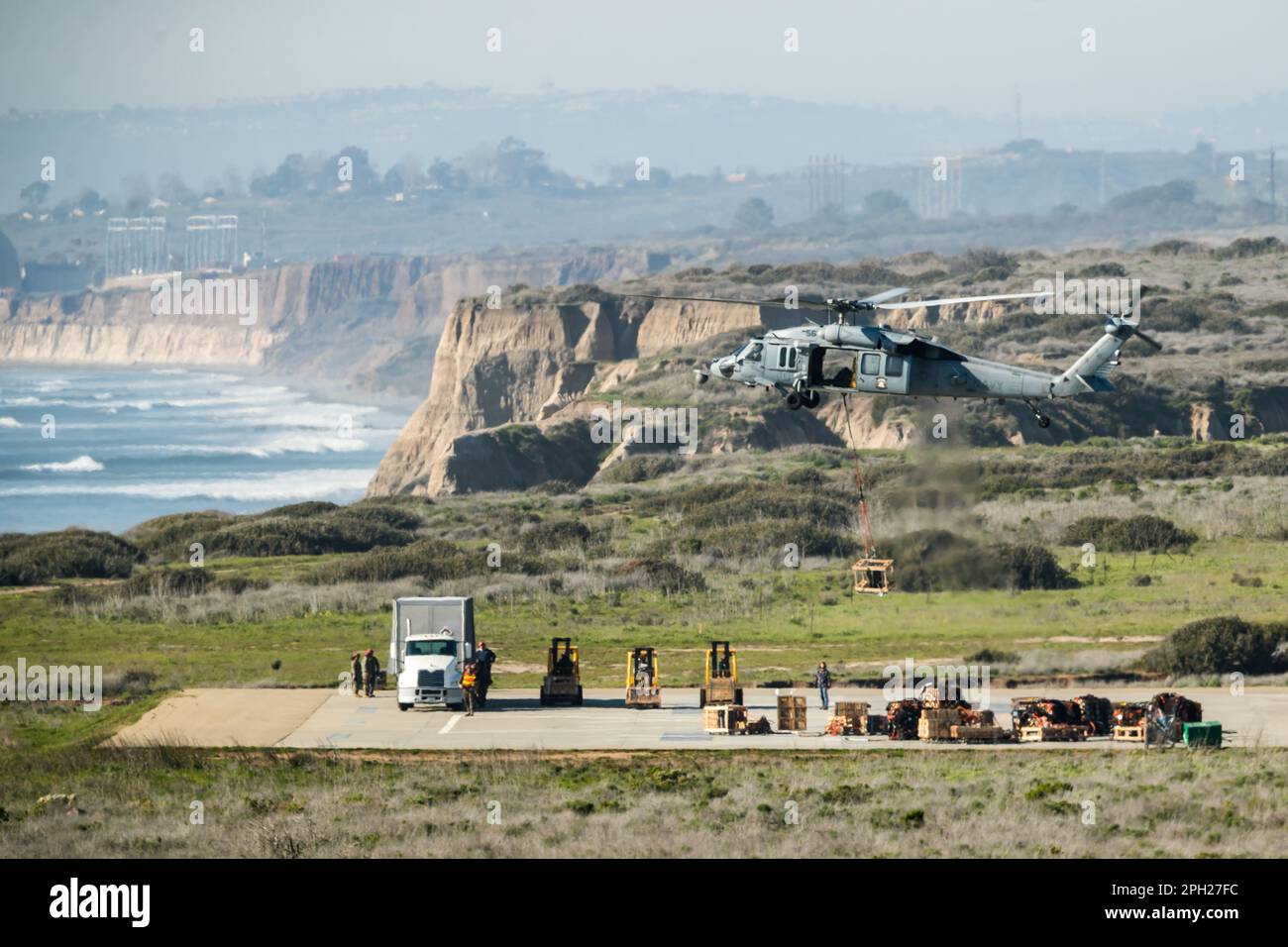 DIE US Navy MH60S fliegt zwischen einem Versorgungsschiff und der Küste durch Camp Pendleton entlang der kalifornischen Küste. Stockfoto