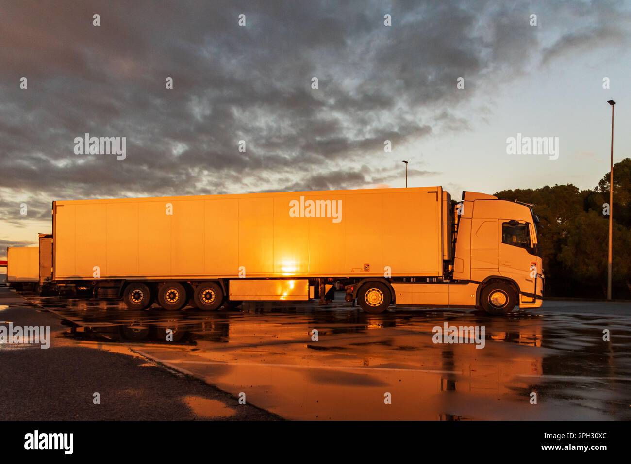Blick auf einen Lkw mit einem gekühlten Auflieger auf einem Parkplatz, auf dem die Abendsonne an der Seite reflektiert wird. Stockfoto
