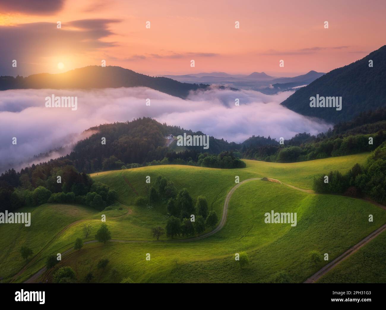 Blick aus der Vogelperspektive auf Bergwiesen und Berge in Wolken bei Sonnenaufgang Stockfoto