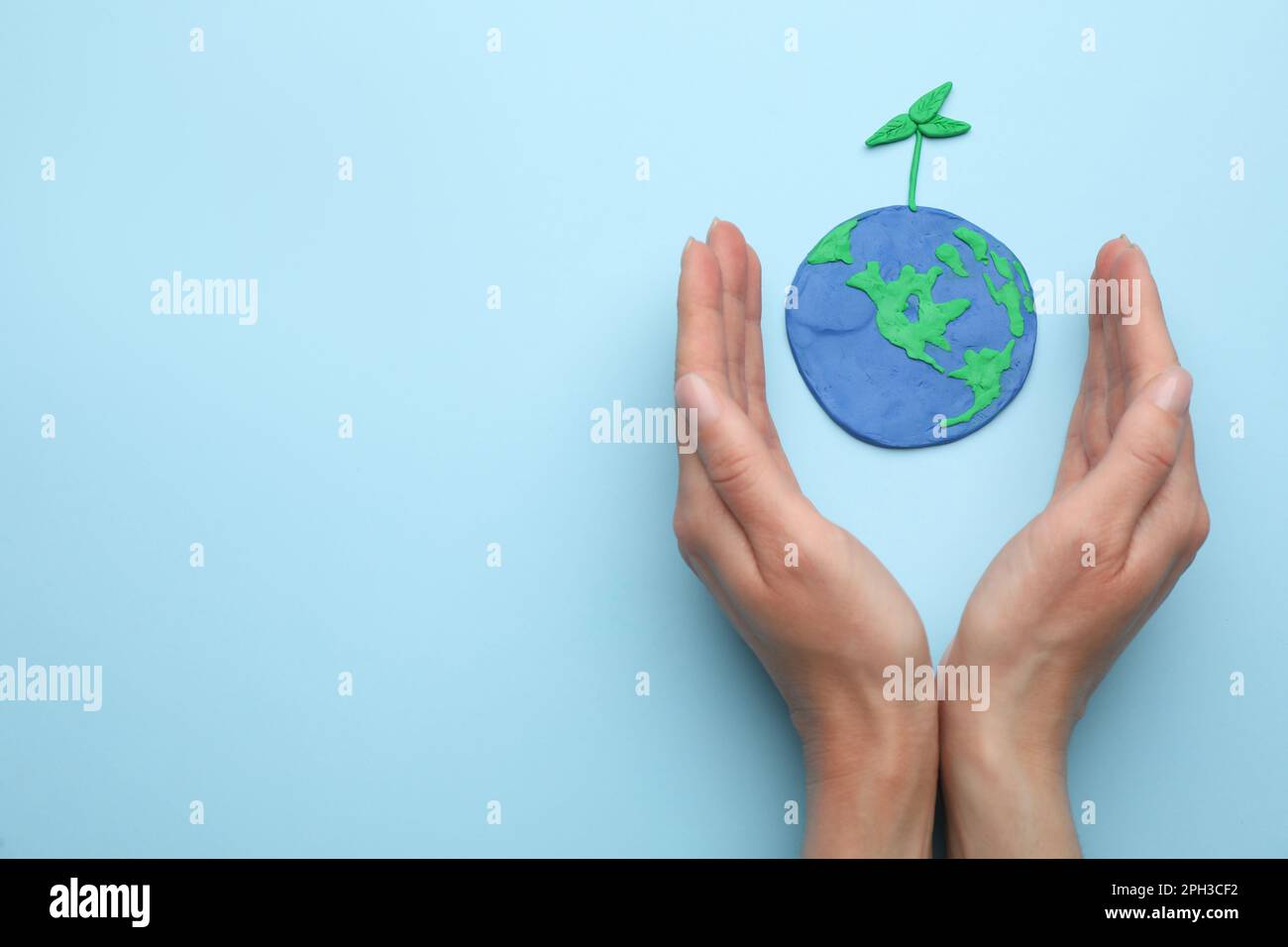 Frau in der Nähe des Plastikinmodells des Planeten mit grünem Setzling und Platz für Text auf hellblauem Hintergrund, Draufsicht. Tag Der Erde Stockfoto