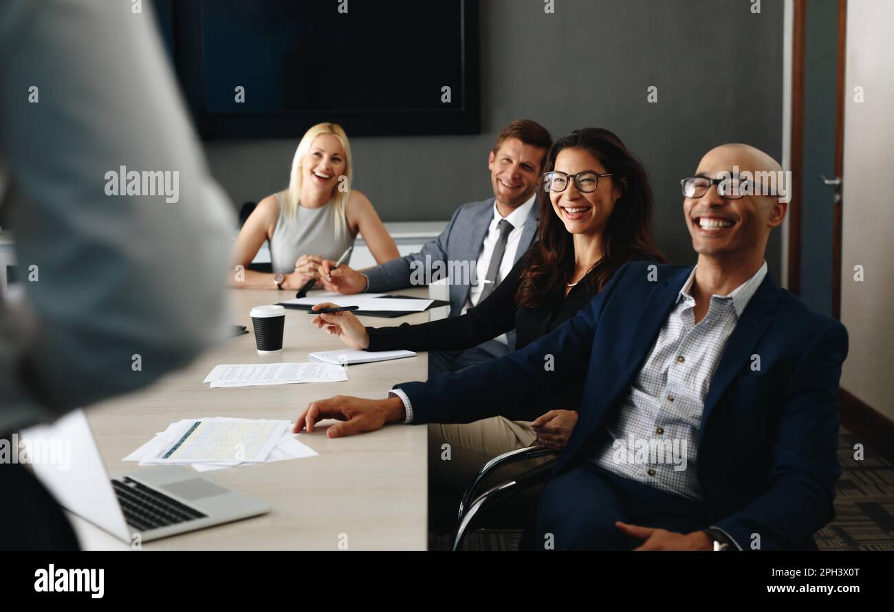 Glückliche Geschäftsleute lächeln, während sie in einem Sitzungssaal sitzen und einer Rede zuhören. Erfolgreiche Unternehmensprofis mit einem Stockfoto