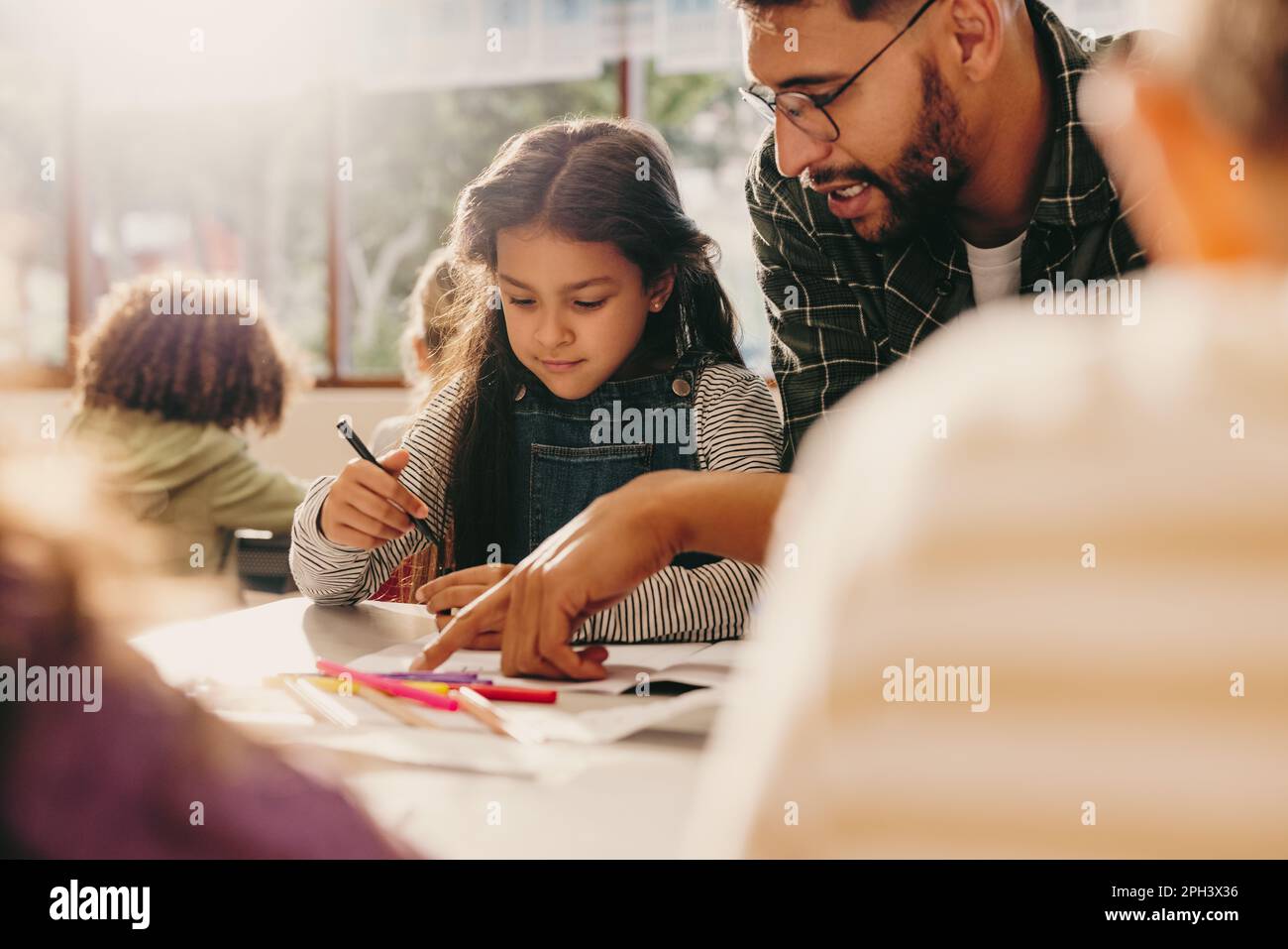 Lehrer, der in einem Kunstunterricht Anleitung gibt. Männlicher Erzieher zeigt einer Schülerin, wie man zeichnet. Männerunterricht und Grundschulklasse. Stockfoto