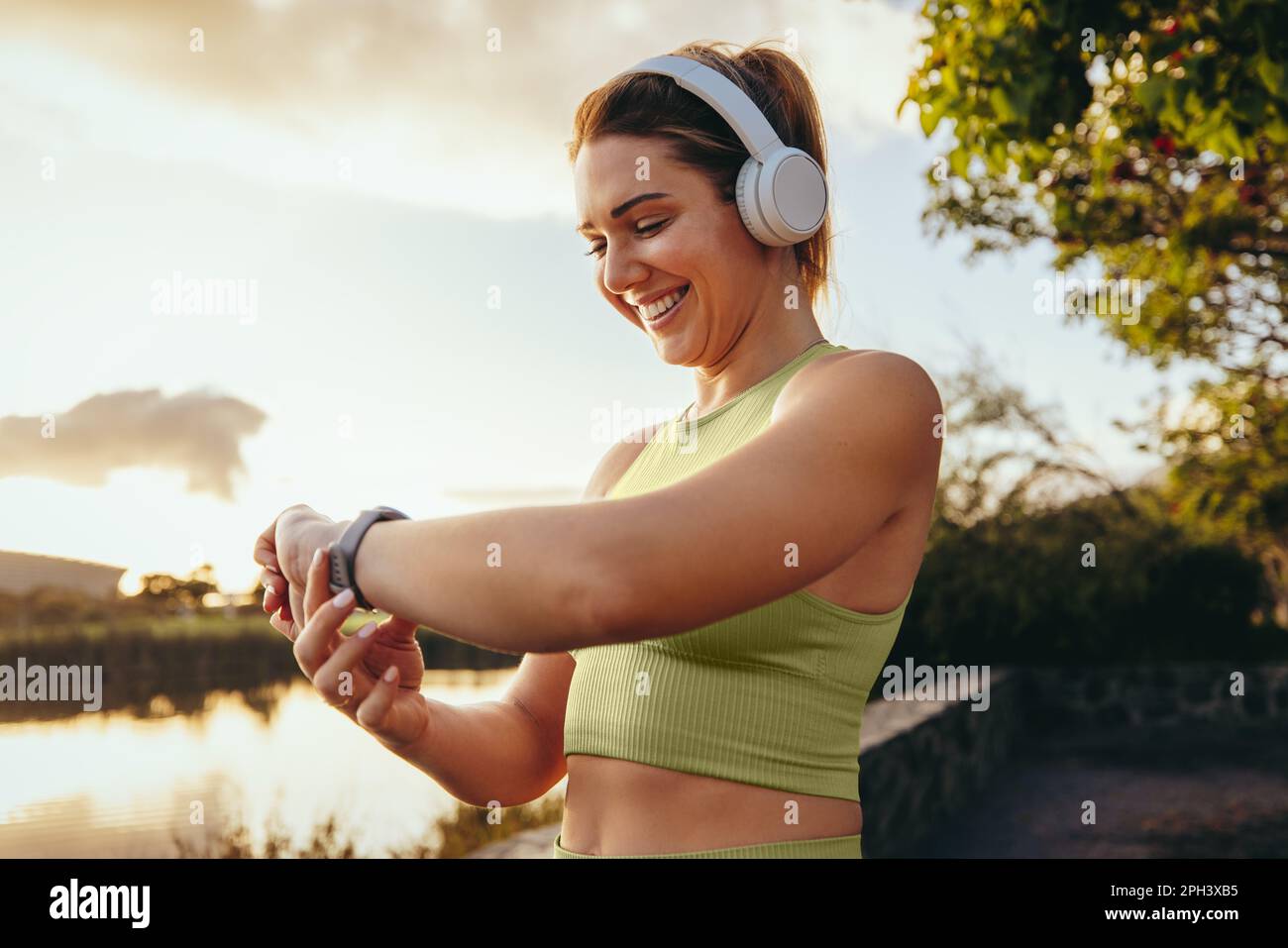 Sportlerin wählt mit einer Smartwatch im Freien eine Fitness-Playlist aus. Glückliche Frau, die mit Kopfhörern einen morgendlichen Lauf macht. Frau, die Technologie für verwendet Stockfoto