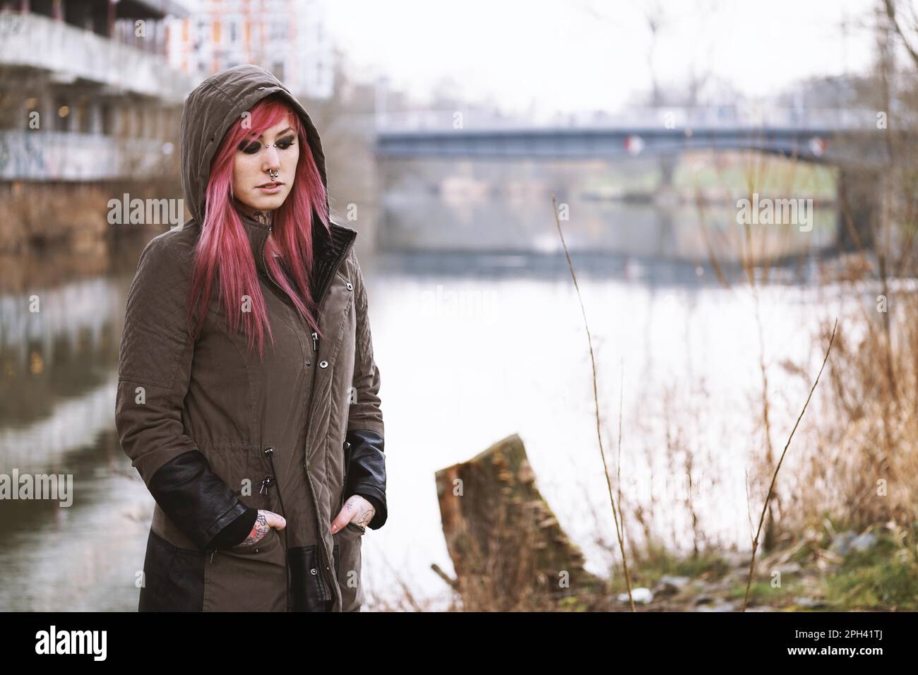 Depressive und einsame junge Frau, die am Fluss in einer düsteren Umgebung steht Stockfoto