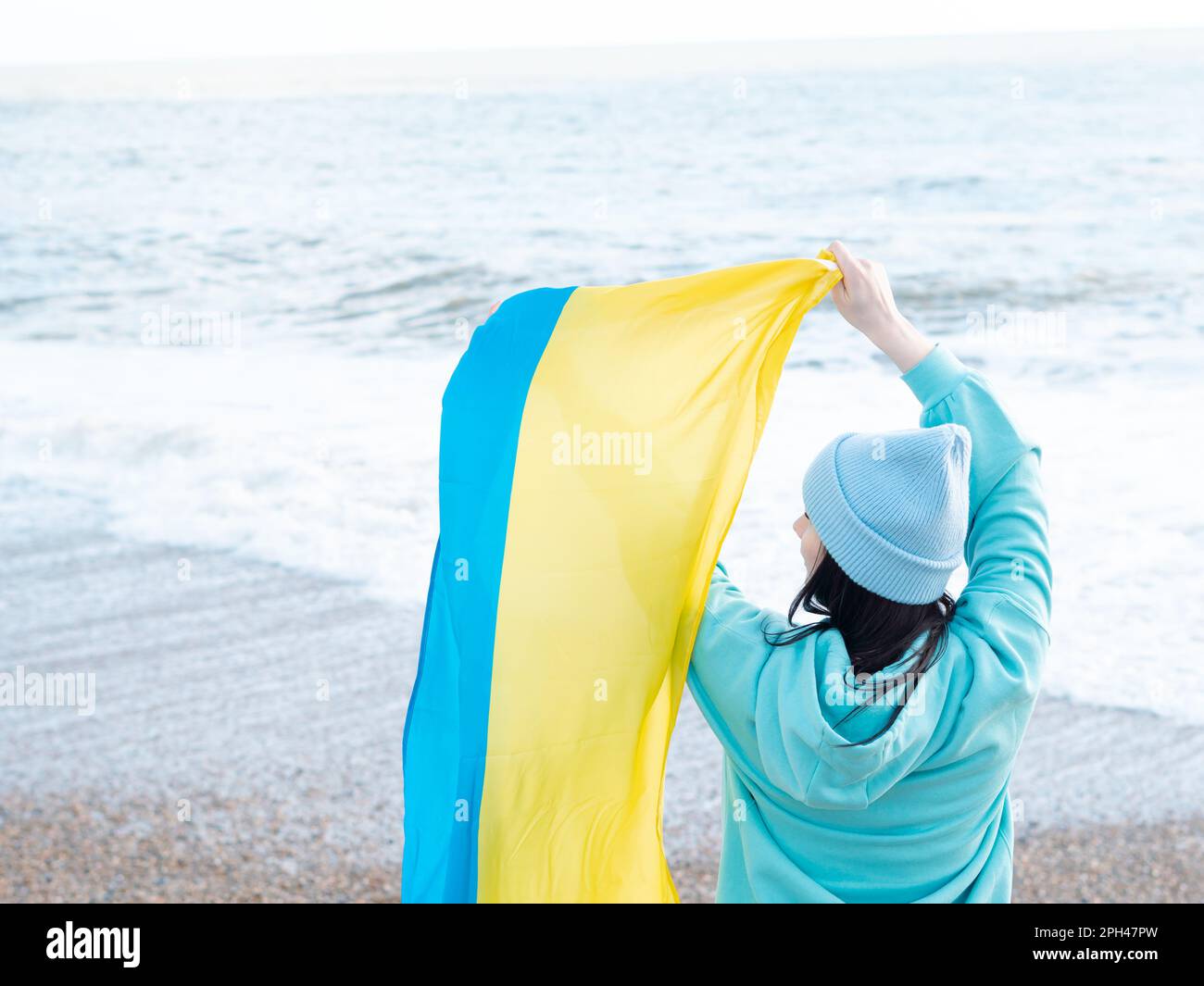 Braune Frau in blauem Hoodie und blauem Hut mit ukrainischer Nationalflagge, patriotisches Konzept Stockfoto