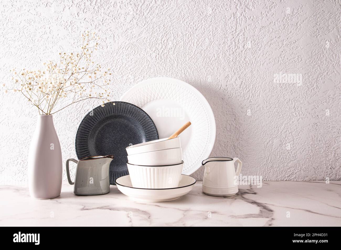 Wunderschöner weißer, stilvoller Hintergrundteil der Küchenarbeitsfläche mit Keramikschüsseln, Tellern und einer Blumenvase. Ein Kopierbereich Stockfoto