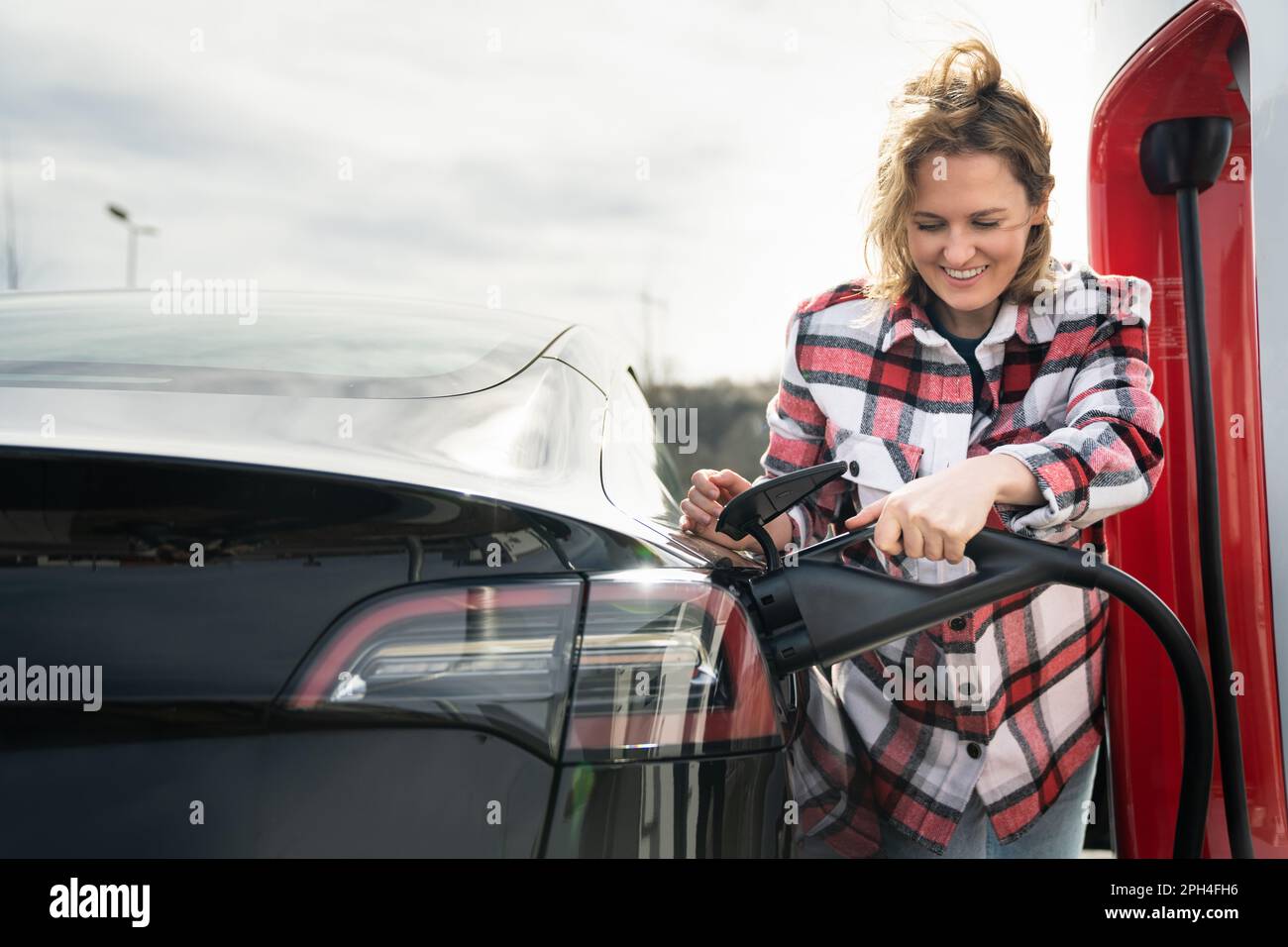 Eine Frau in einem karierten Hemd lädt ein Elektroauto auf. Stockfoto