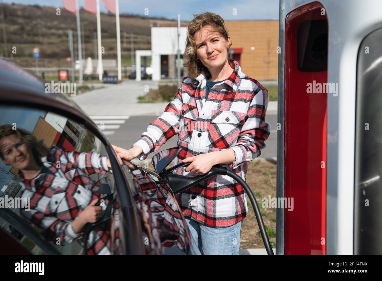 Eine Frau in einem karierten Hemd lädt ein Elektroauto auf. Hochwertiges Foto Stockfoto