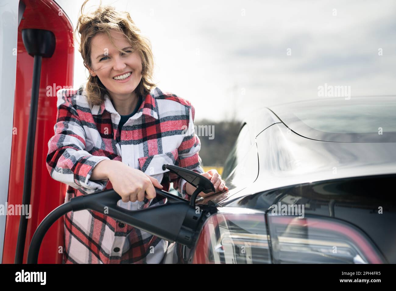 Eine Frau in einem karierten Hemd lädt ein Elektroauto auf. Hochwertiges Foto Stockfoto