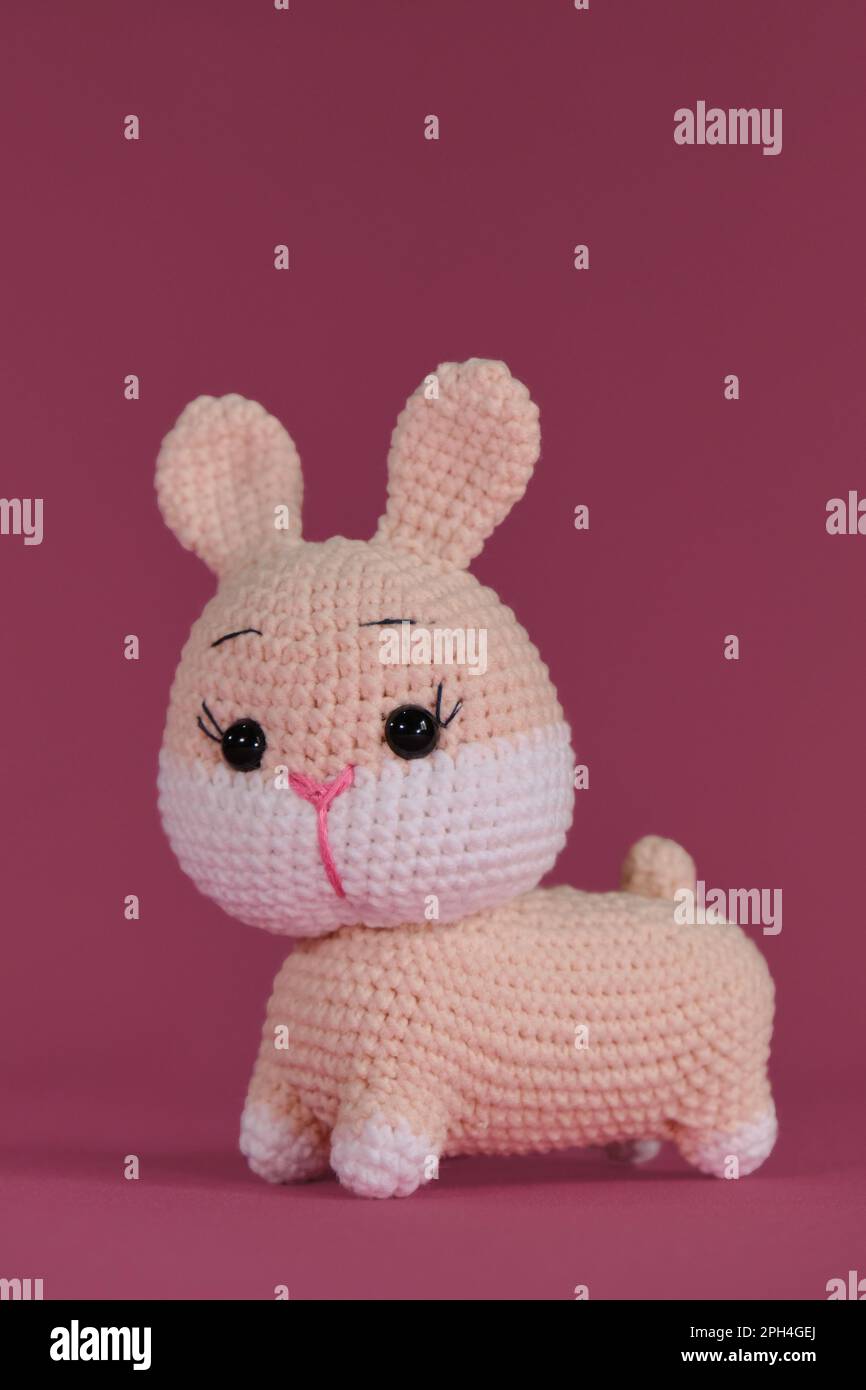 Konzeptsymbol katholischer Ostern. Rosa niedliches Osterhasen gestrickt, handgemachte Kunst. Amigurumi Hase Puppe auf pinkfarbenem Hintergrund. Weiches Heimwerkerspielzeug aus Cott Stockfoto