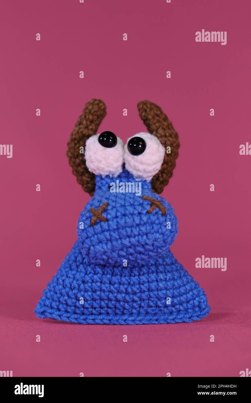 Amigurumi, ein kleiner blauer Stier mit braunen Hörnern auf rosa Hintergrund. Vorderansicht. Weiches Spielzeug aus natürlicher Baumwolle und Wolle. Kuhkopf gehäkelt, Hand Stockfoto