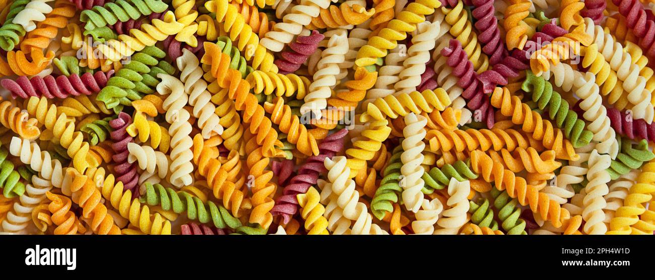 Farbige italienische Pasta auf weißem Hintergrund. Kinderpaste mit natürlichen Farbstoffen aus Gemüse und Kräutern. Pasta Hintergrund.Banner. Stockfoto