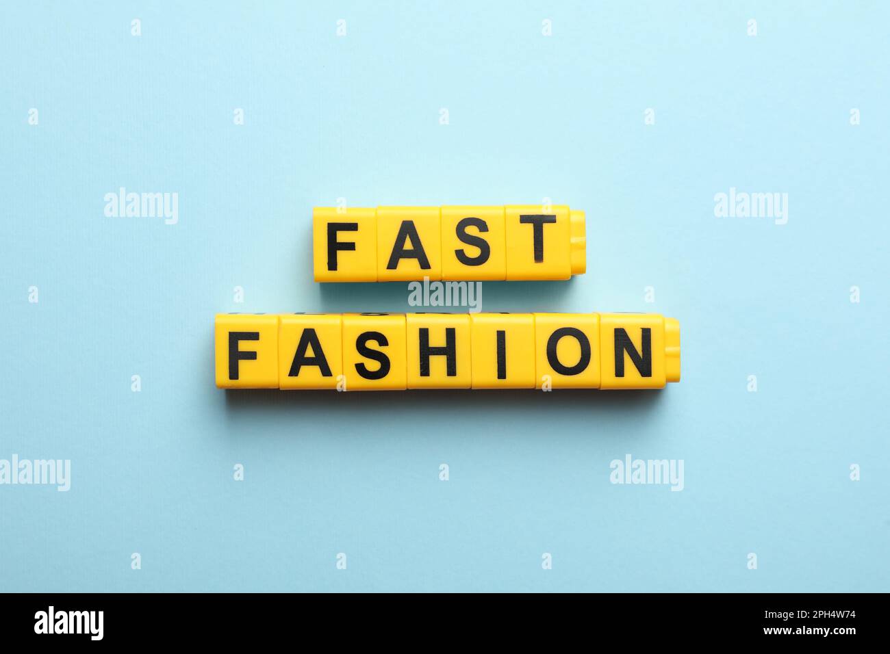 Gelbe Kunststoffwürfel mit der Phrase „Fast Fashion“ auf hellblauem Hintergrund, flach liegend Stockfoto