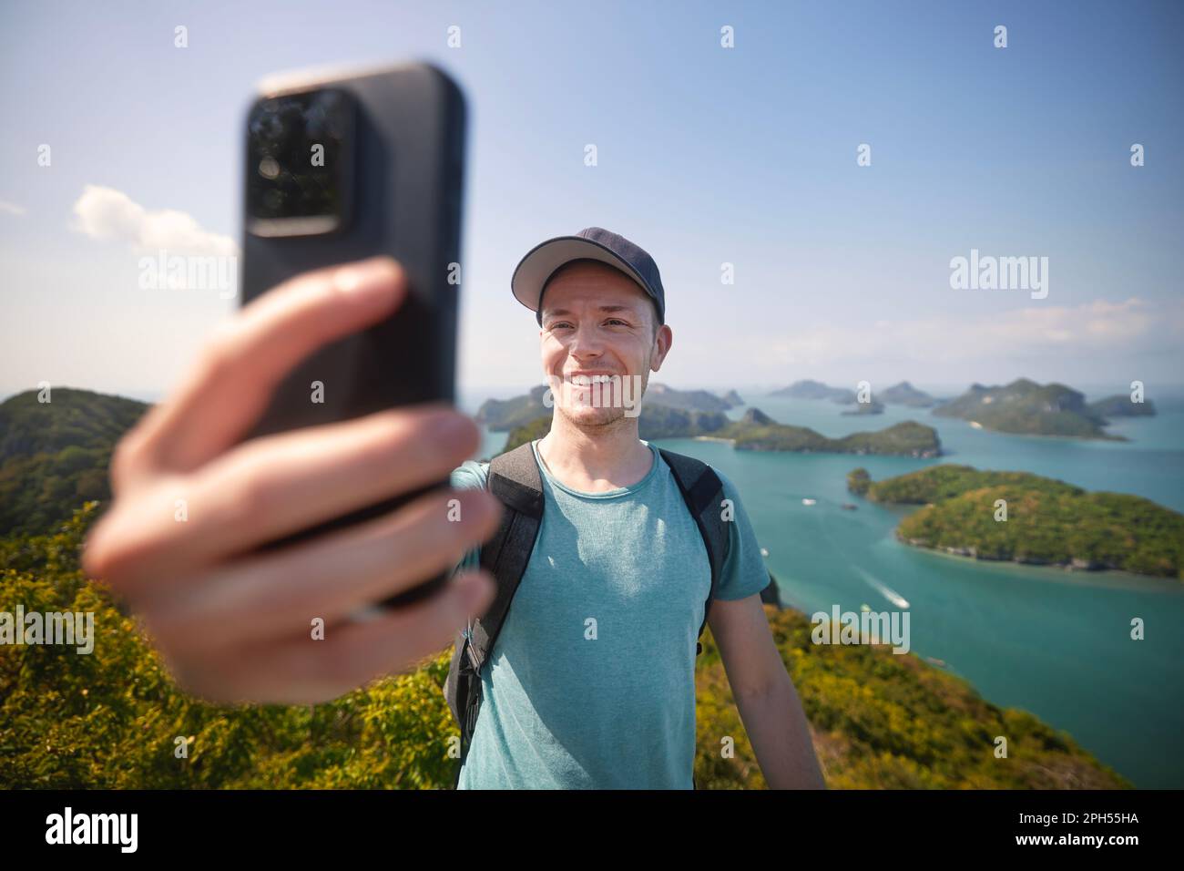 Lächelnder Mann mit Rucksack, der Selfie-Porträt auf dem Hügel gegen eine Gruppe tropischer Inseln im Meer macht. Ang Thong National Marine Park in der Nähe von Koh Samui in Th Stockfoto