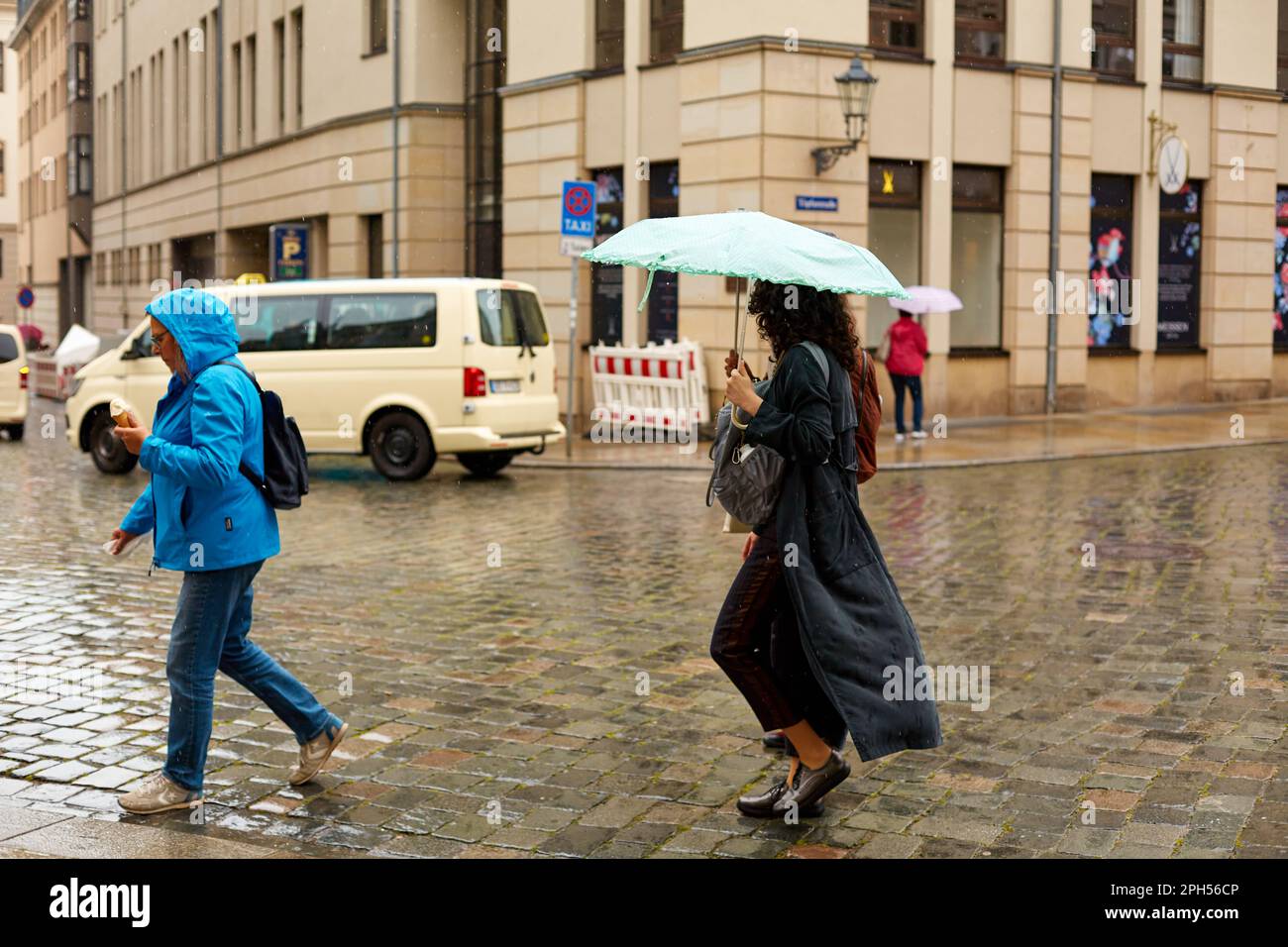 Menschen mit Sonnenschirmen laufen im Regen durch eine europäische Stadt. Dresden, Deutschland - 05.20.2019 Stockfoto