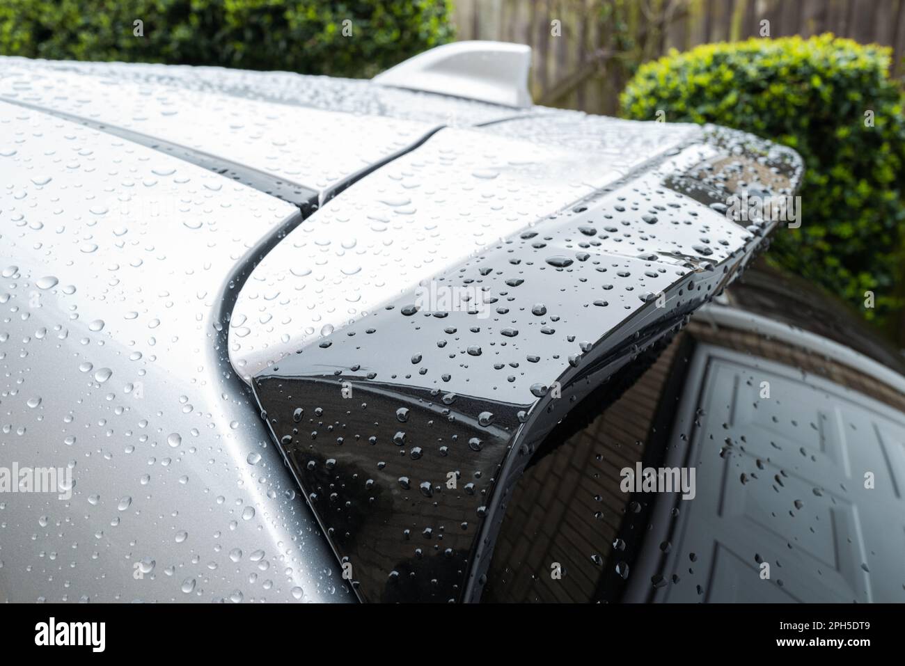 Flacher Fokus von Wassertropfen auf dem Dachspoiler eines modernen Hybrid-City-Autos. Nach einer Autowaschanlage befindet sich das Auto in einer Einfahrt. Stockfoto