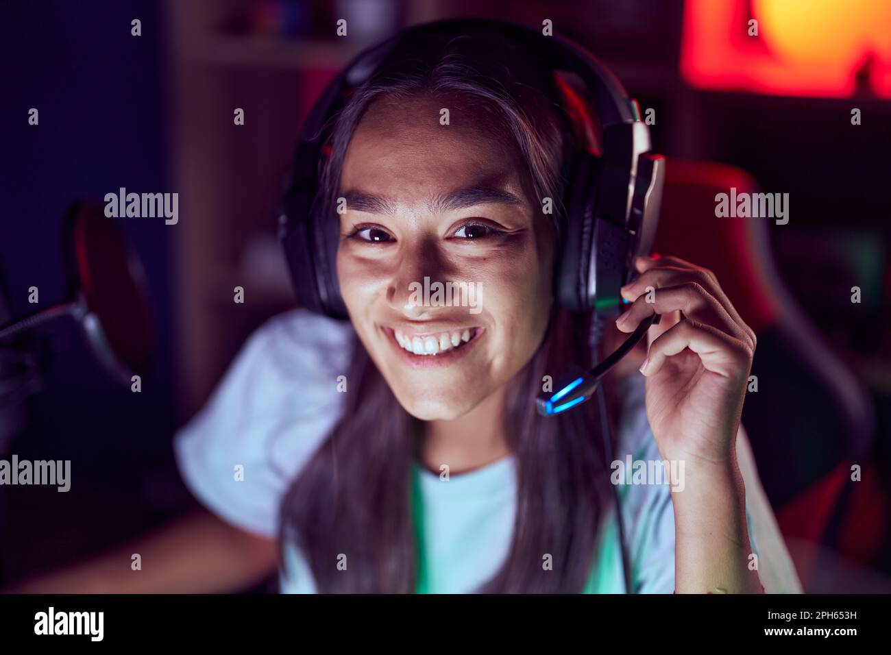 Junge schöne hispanische Frau streamer lächelnd selbstbewusst auf dem Tisch im Spielzimmer sitzen Stockfoto