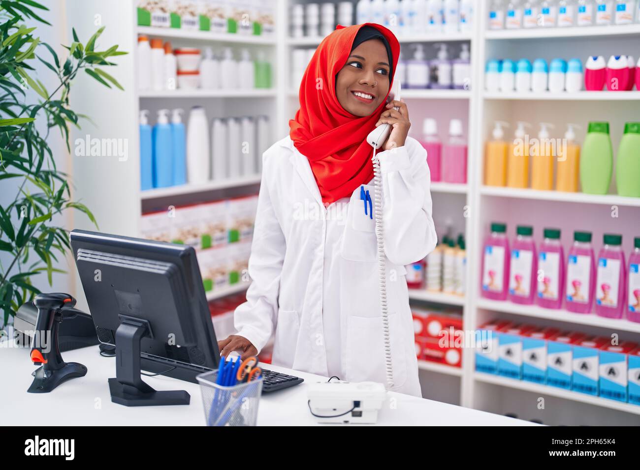 Eine junge, schöne Apothekerin, die telefoniert, indem sie einen Computer in der Apotheke benutzt Stockfoto