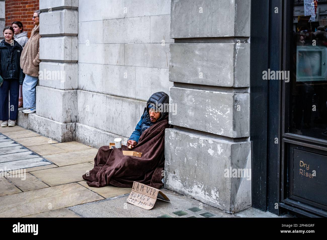 Ein obdachloser Mann sitzt auf dem Bürgersteig mit einem Schild und bittet um Hilfe. Central London, England, Großbritannien Stockfoto