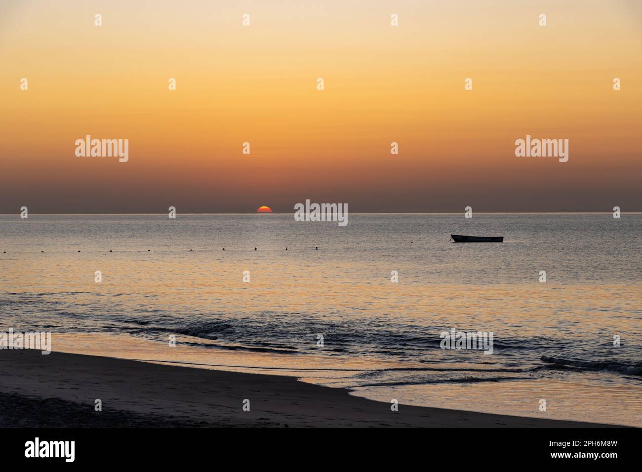 Sonnenaufgang an der Westküste von Panama. Die Sonne erhebt sich über dem Horizont mit einem leeren Boot, das auf dem Wasser schwimmt. Orangefarbener Himmel und die Sonne beginnt zu erscheinen. Stockfoto