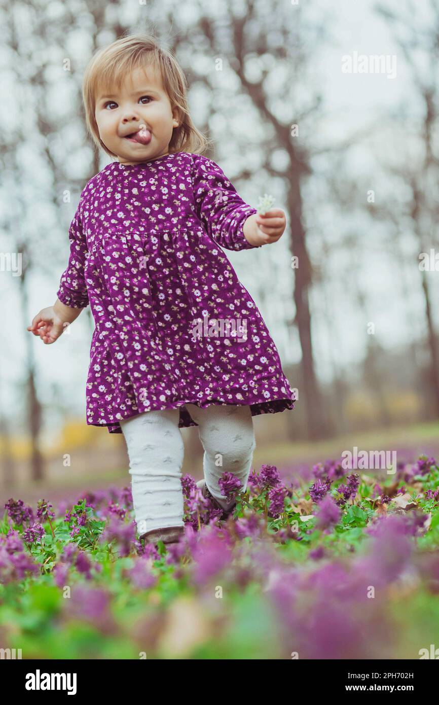 Das Baby in einem farbigen Kleid läuft mit der Zunge im Wald herum Stockfoto