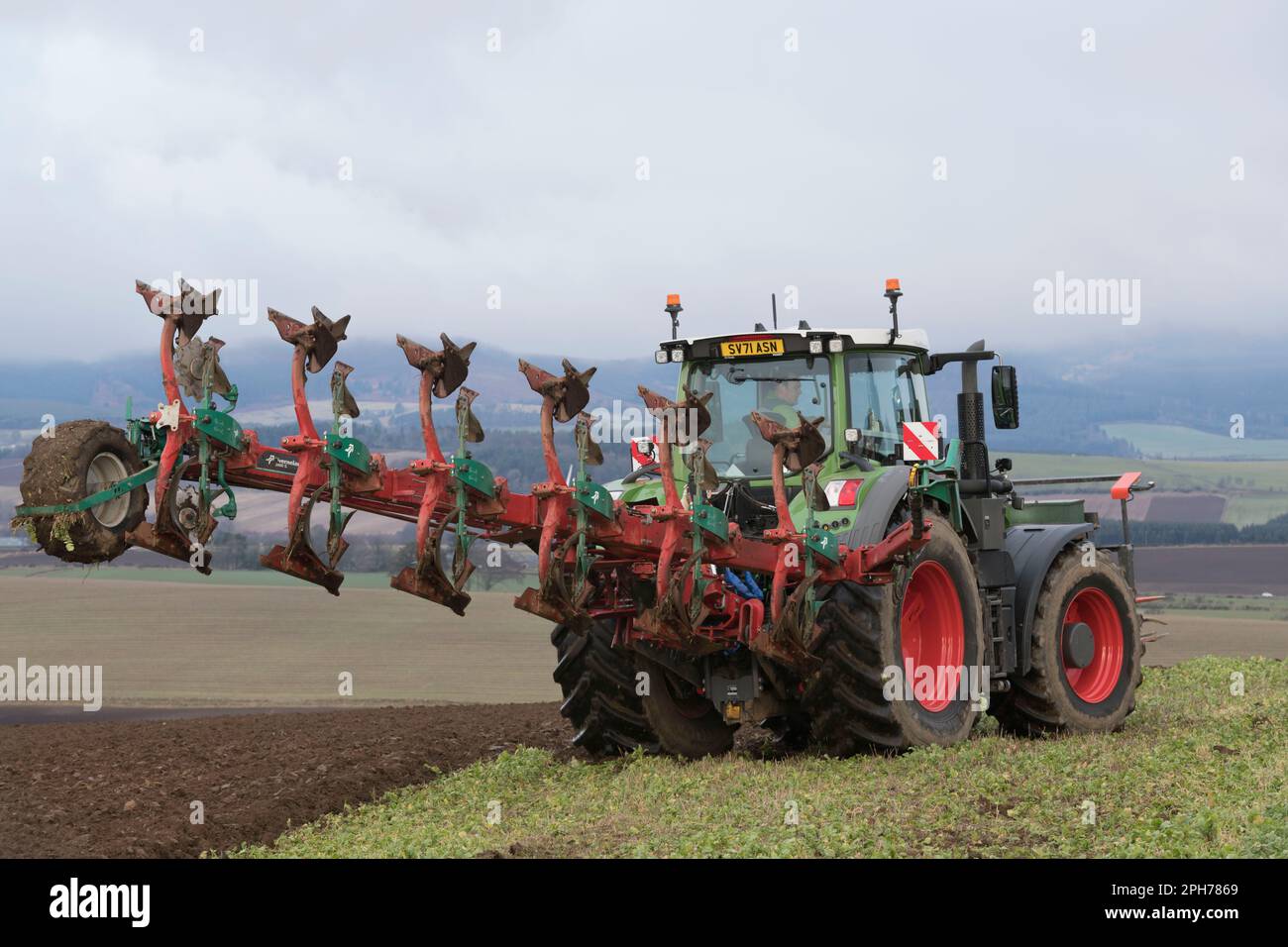 Ein Fendt Traktor mit einem Kverneland Variomat 3400 S Wendepflug auf einem Wiesenfeld (Gründung) während des Pflügen im Frühjahr Stockfoto