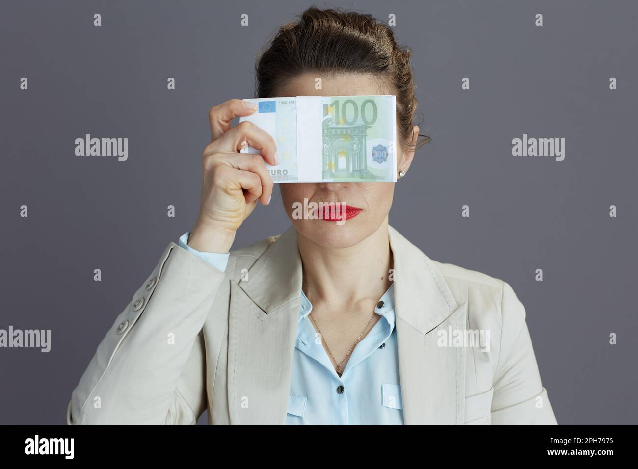 Trendige 40-jährige Geschäftsfrau in einem leichten Business-Anzug mit Euro-Geldbeuteln, die zeigen, dass keine böse Geste auf grauem Hintergrund isoliert ist. Stockfoto