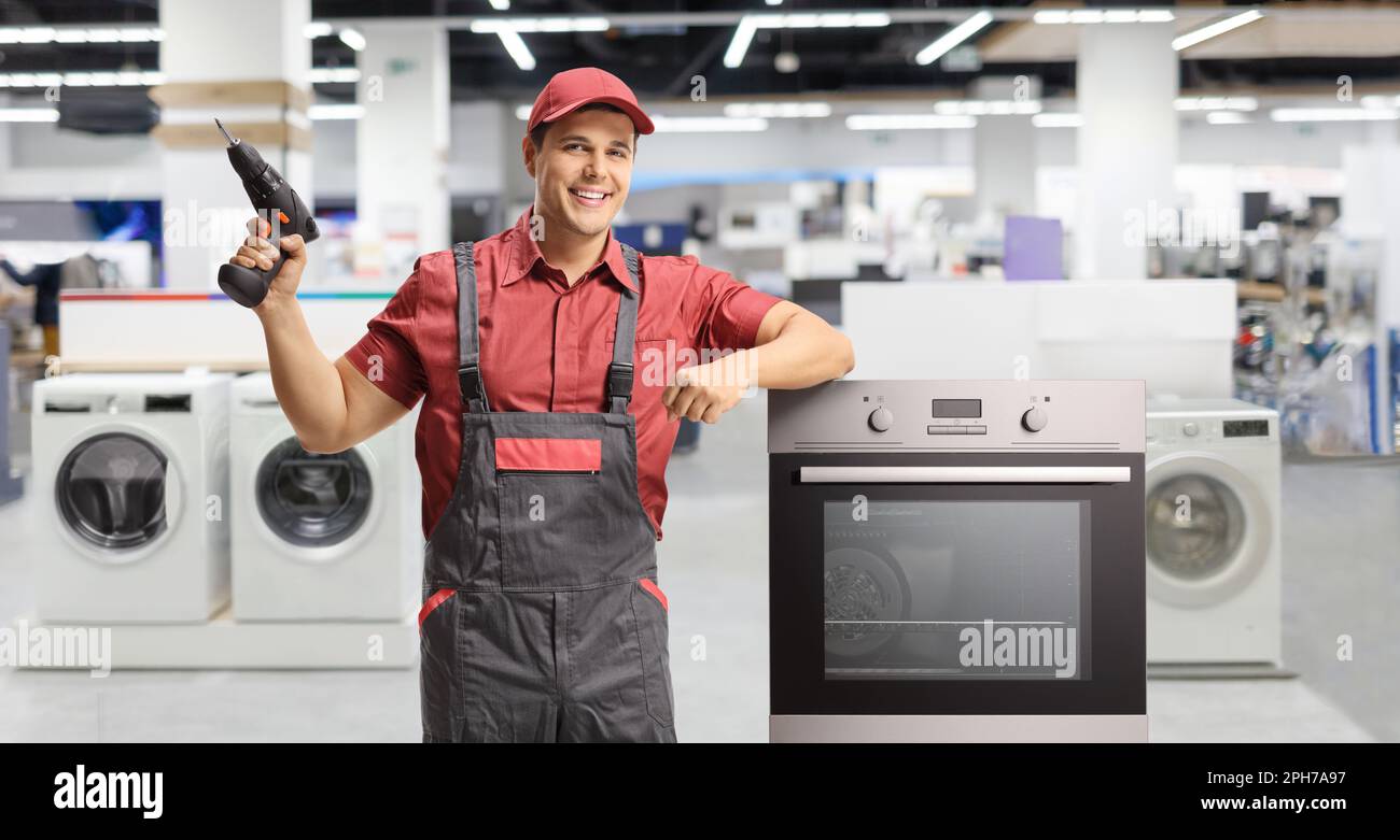 Ein Techniker mit einer Elektrobohrmaschine steht neben einem Ofen in einer Haushaltswerkstatt Stockfoto