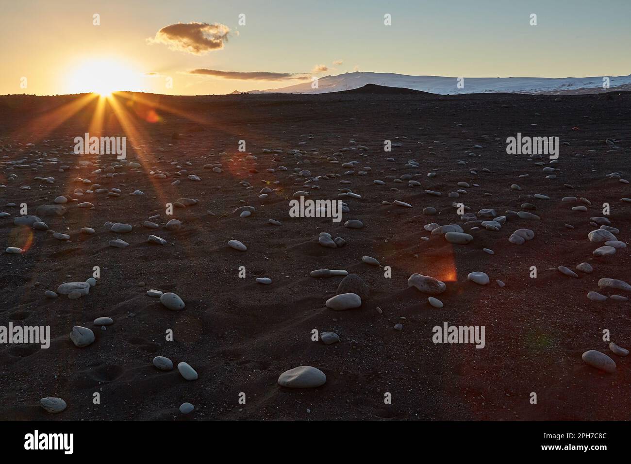 Island Landschaft schwarzen Sandstrand mit Steinen und Sonnenuntergang Flare Stockfoto