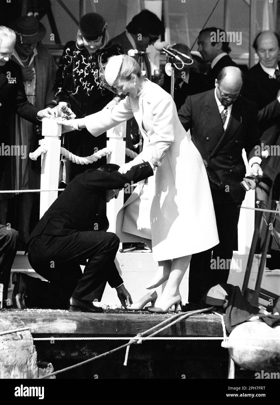 AJAXNETPHOTO. 26TH. MÄRZ 1982. KÜHE, ENGLAND. AMERICA'S CUP YACHT LAUNCH - H.R.H. PRINZESSIN MICHAEL VON KENT WURDE ANMUTIG AN LAND UND IN IHRE SCHUHE NACH EINER BARFUSS-TOUR DER YACHT, DIE SIE GERADE BENANNT HATTE, GEBRACHT, WÄHREND DER SIEGESEIDIGE KAUFMANNSBANKER PETER DE SAVARY (RECHTS) MIT SEINEN BROGUES HERUMFUMMELT. DIE PRINZESSIN SCHEINT MR. DE SAVARYS DILEMMA AMÜSANT ZU FINDEN. FOTO: JONATHAN EASTLAND/AJAX REF:222904 MX340 17 (SIEHE AUCH 222904 MX340 18 & 19) Stockfoto