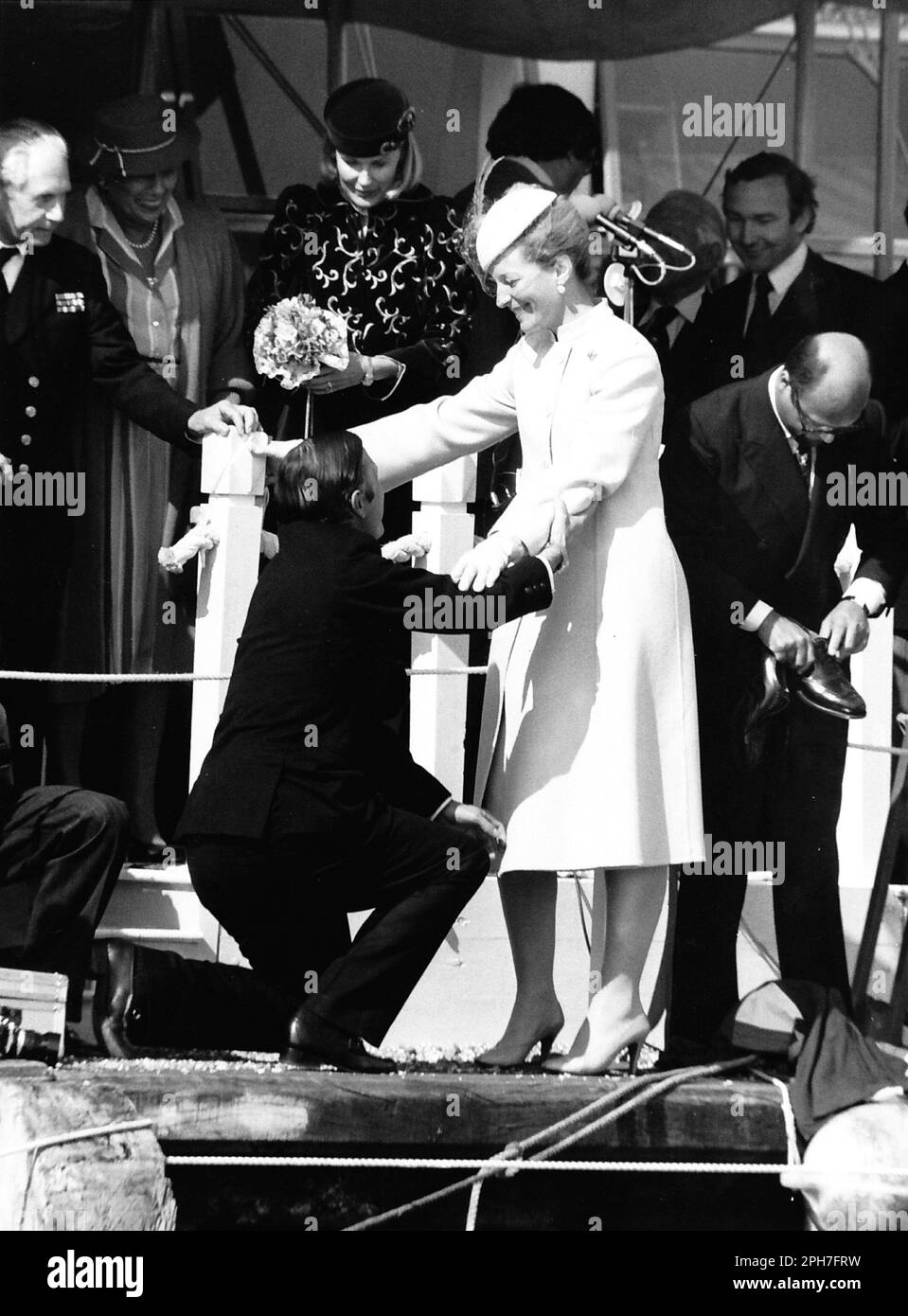 AJAXNETPHOTO. 26TH. MÄRZ 1982. KÜHE, ENGLAND. AMERICA'S CUP YACHT LAUNCH - H.R.H. PRINZESSIN MICHAEL VON KENT WURDE ANMUTIG AN LAND UND IN IHRE SCHUHE NACH EINER BARFUSS-TOUR DER YACHT, DIE SIE GERADE BENANNT HATTE, GEBRACHT, WÄHREND DER SIEGESEIDIGE KAUFMANNSBANKER PETER DE SAVARY (RECHTS) MIT SEINEN BROGUES HERUMFUMMELT. DIE PRINZESSIN SCHEINT MR. DE SAVARYS DILEMMA AMÜSANT ZU FINDEN. FOTO: JONATHAN EASTLAND/AJAX REF:222904 MX340 18 (SIEHE AUCH 222904 MX340 17 & 19) Stockfoto