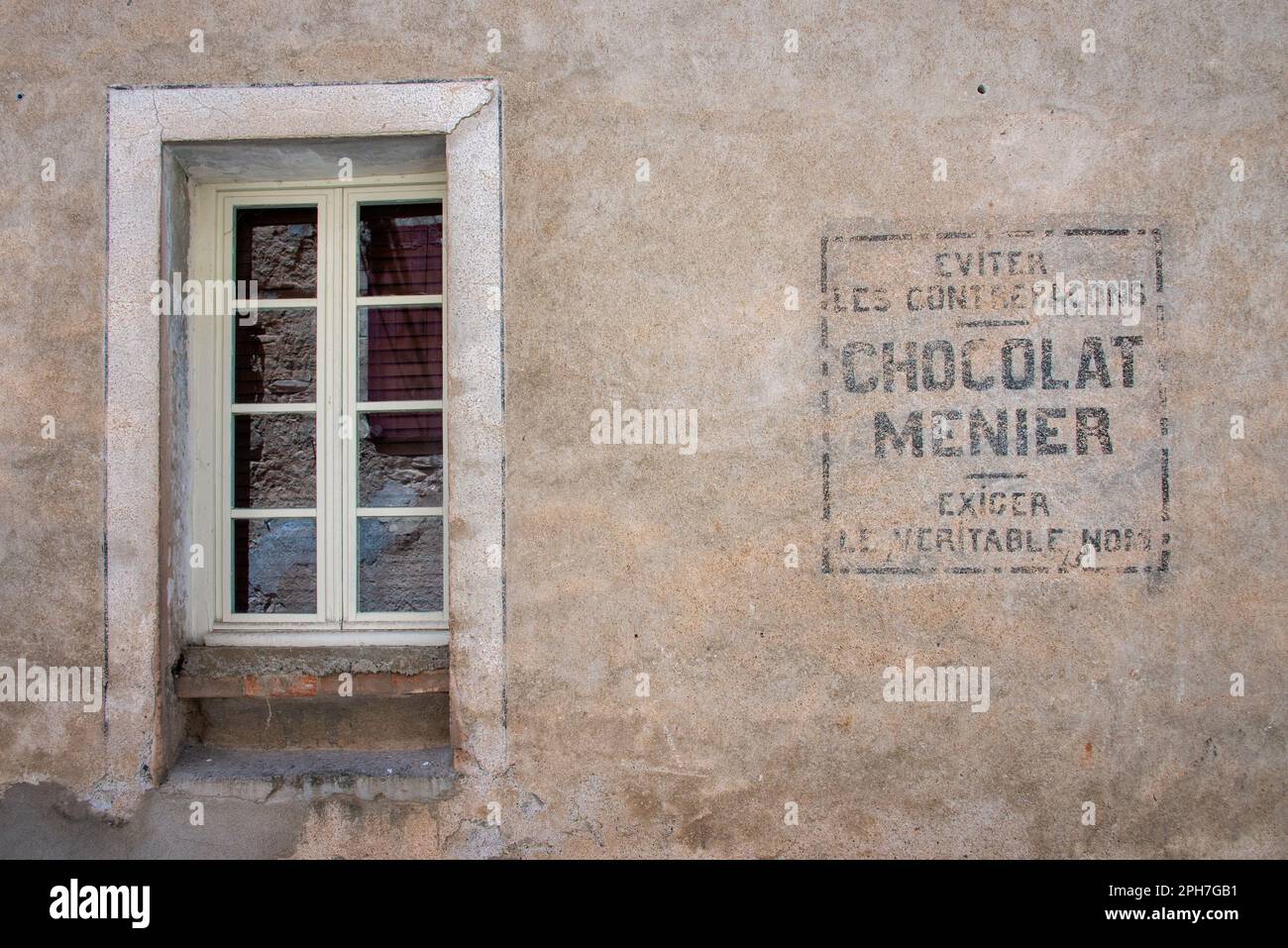 Chocolat Menier: Ein verblichenes Zeichen einer vergessenen Süßwarenmarke an einer Fassade im alten Dorf Roquebrun im Orb-Flusstal Südfrankreichs. Stockfoto