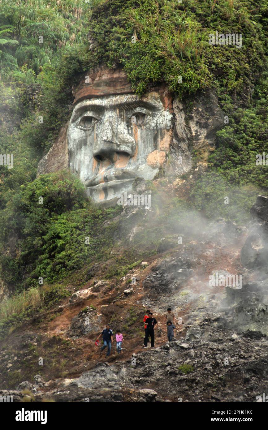 Die Besucher haben Freizeit auf dem Fumarole Field, vor dem Hintergrund einer riesigen Gesichtsformation, die den Charakter von Toar, der – zusammen mit Lumimuut – zeigt Sie werden als die Vorfahren der Minahasaner nach lokaler Mythologie im Bukit Kasih, einem beliebten Ziel für Kultur-, Natur- und religiösen Tourismus im Dorf Kanonang, West Kawangkoan, Minahasa, North Sulawesi, Indonesien, angesehen. Stockfoto