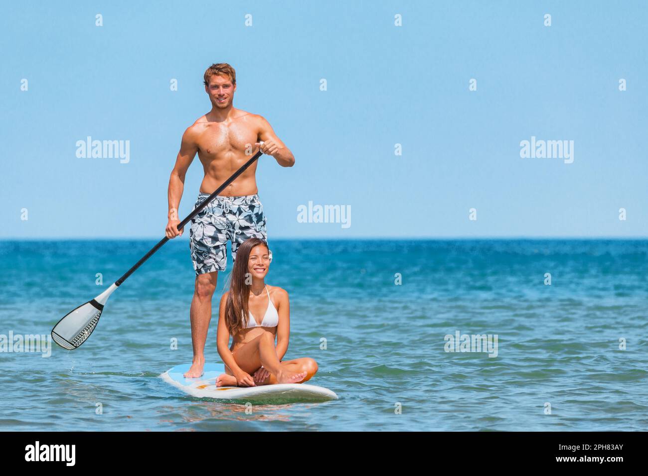 Aufblasbare Stand-Up-Paddle-Board Wassersportaktivitäten für Paare. Paare Touristen, die Spaß beim Paddeln haben, mit Strandverleih Sportausrüstung für SUP Stockfoto