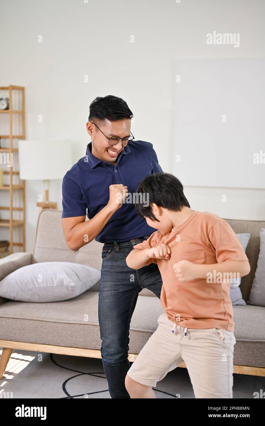 Fröhlicher und verspielter asiatischer Vater und kleiner Sohn, die zusammen im Wohnzimmer tanzen, Spaß mit der Familie haben, glücklichen alleinerziehenden Vater und Sohn. Stockfoto