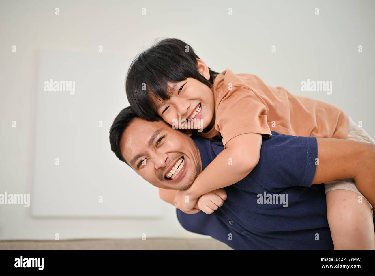 Glücklicher asiatischer Sohn und Vater, die sich zu Hause amüsieren, im Wohnzimmer spielen und Huckepack spielen. Glückliche Familie und alleinerziehender Vater Konzept Stockfoto