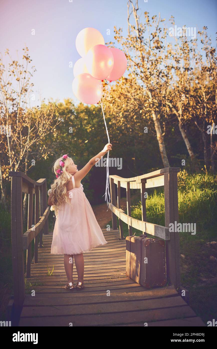 Ballons machen mich glücklich. Ein glückliches kleines Mädchen, das Ballons und einen Teddybär hält, während es mitten auf einer Brücke steht. Stockfoto