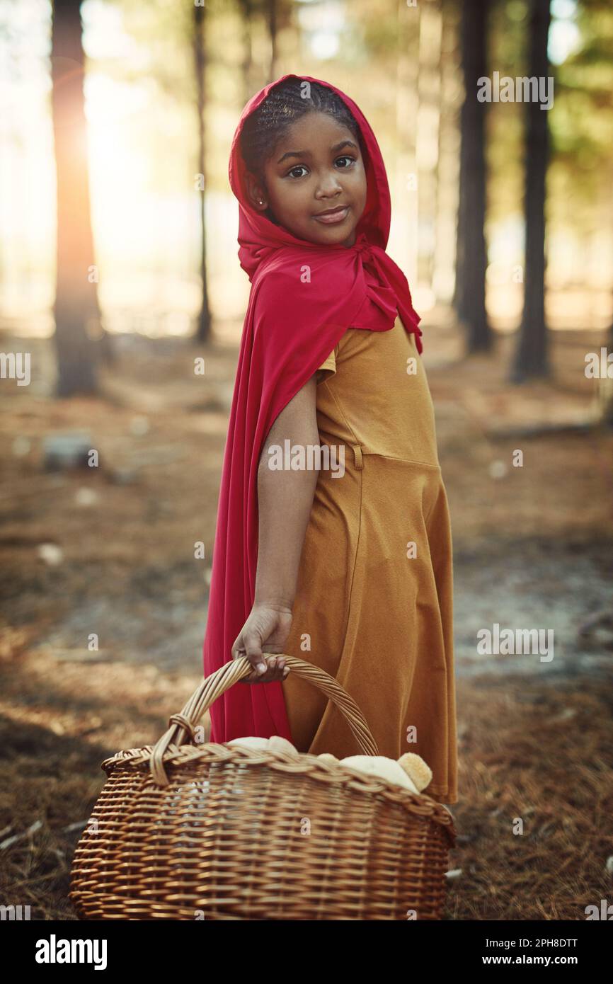 Sie hat eine kleine rote Reithaube. Porträt eines kleinen Mädchens in einem roten Umhang und mit einem Korb im Wald. Stockfoto