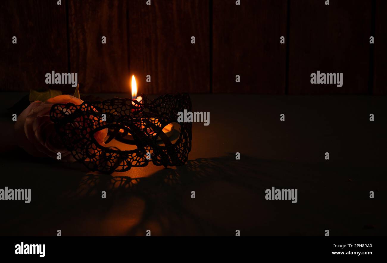 Kerzenflamme und neben einer Rose und Spitze Gesichtsmaske für Karneval im Dunkeln Nahaufnahme Stockfoto