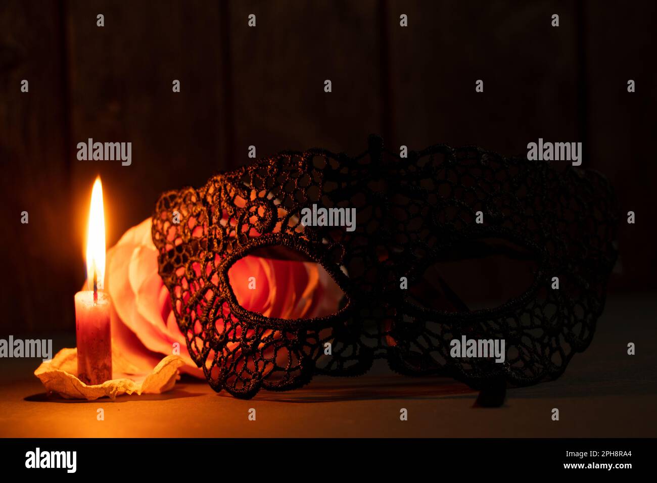 Eine Kerzenflamme und neben einer Rose in der dunklen Nahaufnahme Stockfoto