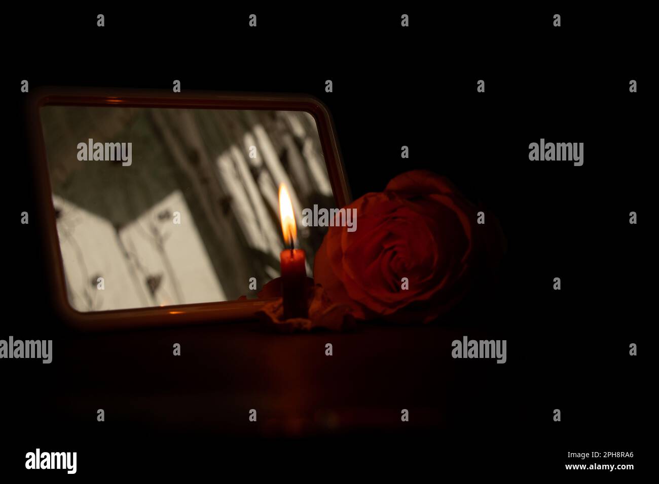 Eine Kerzenflamme und neben einer Rose in der dunklen Nahaufnahme Stockfoto