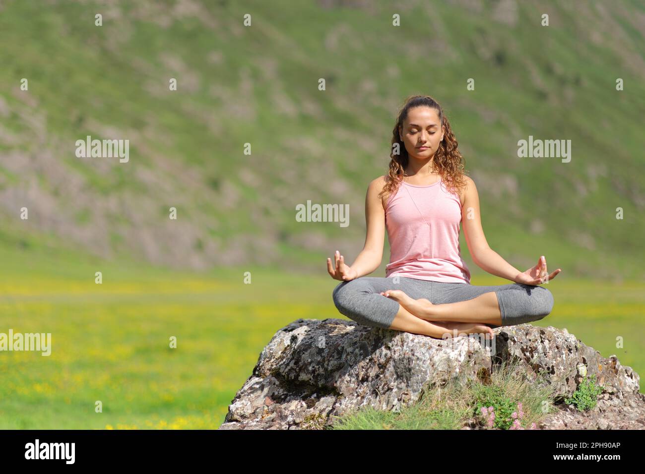 Blick nach vorne, wie ein Yoga-Yoga auf einem Felsen in den Bergen macht Stockfoto
