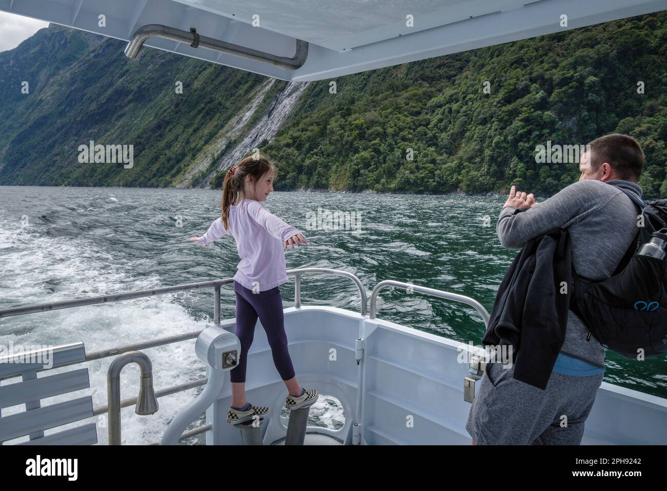 Ein Mädchen, das während einer Bootsfahrt auf dem Milford Sound, South Island, Neuseeland, eine Titanic-Pose für ein Foto macht Stockfoto