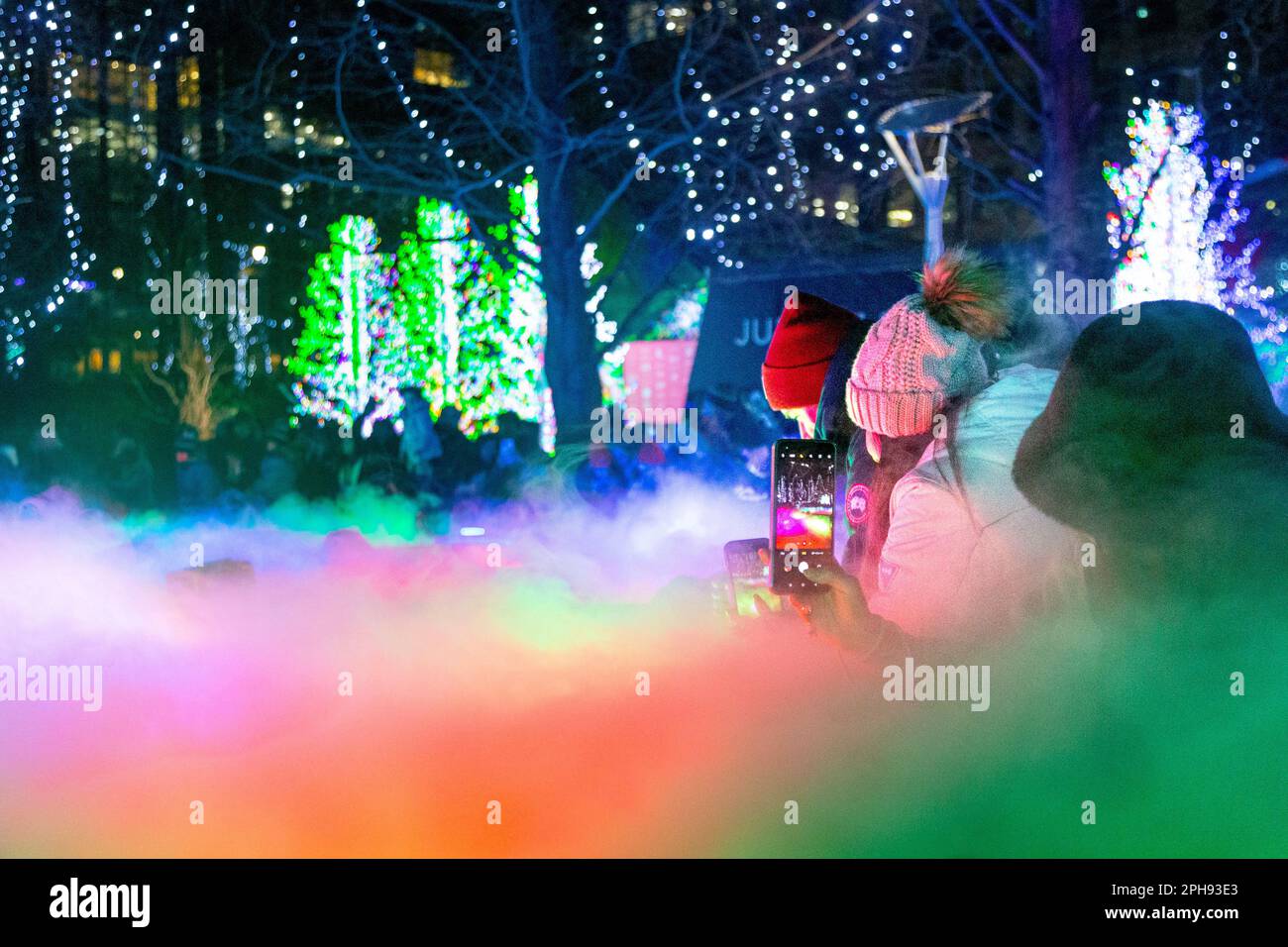 Menschen, die während der Canary Wharf Winter Lights 2023, London, Großbritannien, Fotos von der farbenfrohen Lichtinstallation an den Jubille Park Fountains machen Stockfoto
