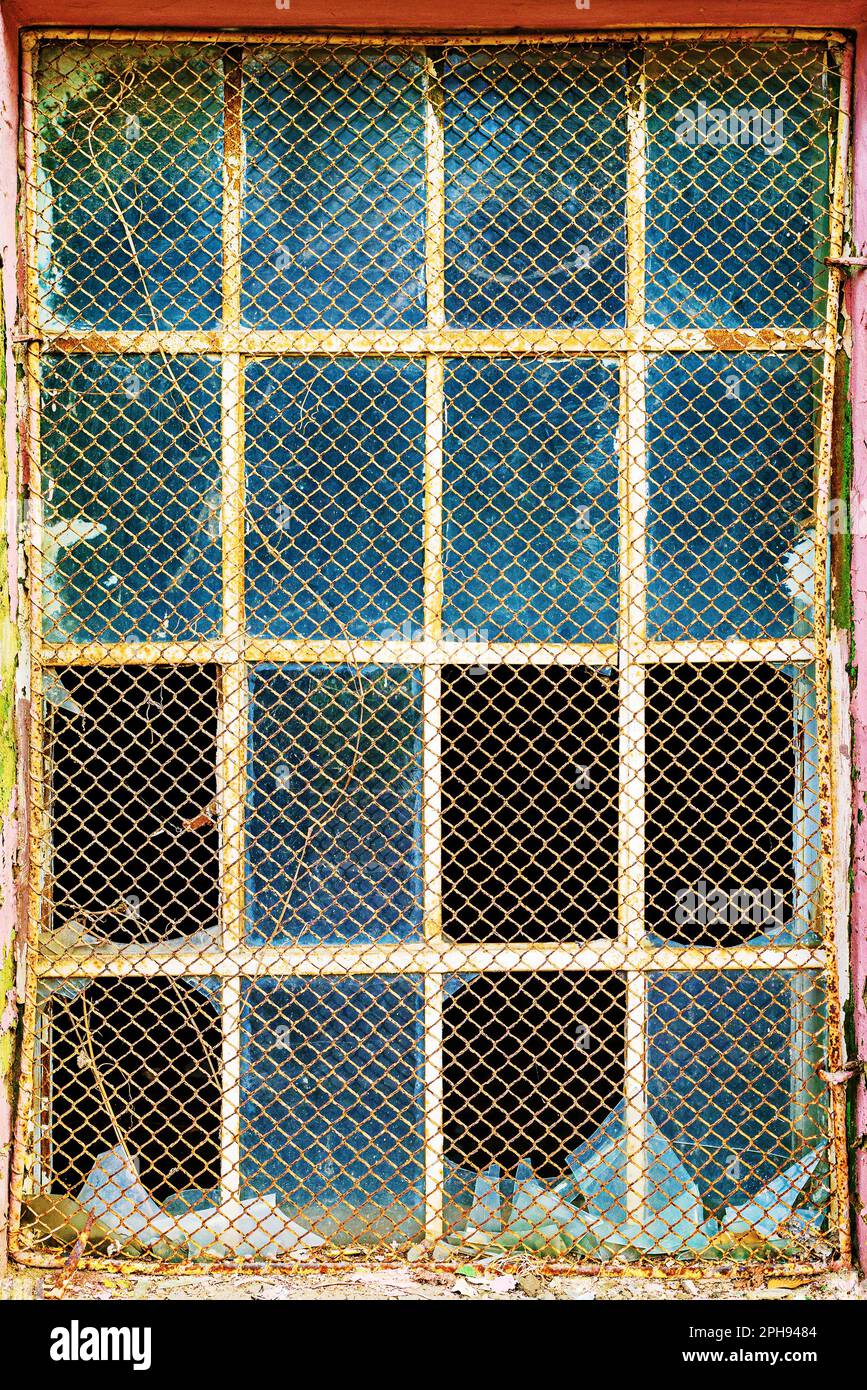 Alte Gitterfenster mit zerbrochenem Glas an der Außenwand eines alten verlassenen Fabriklagers Stockfoto