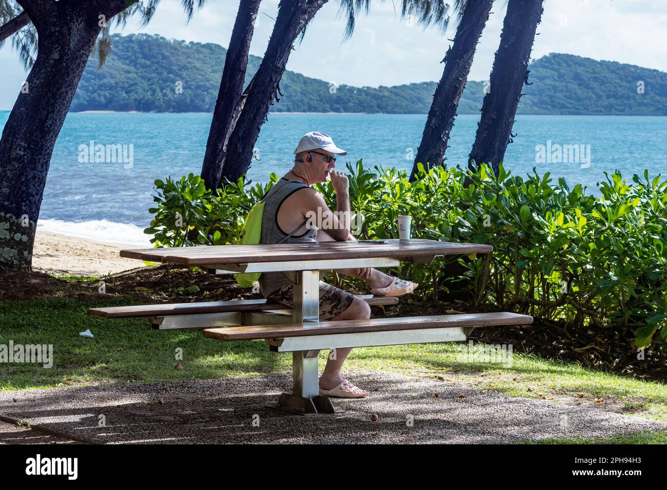 Ein nachdenklicher kausasischer Mann, der die Korallensee auf der Palm Cove Esplanade, Cairns Northern Beaches, Far North Queensland, FNQ, QLD, Australien Stockfoto