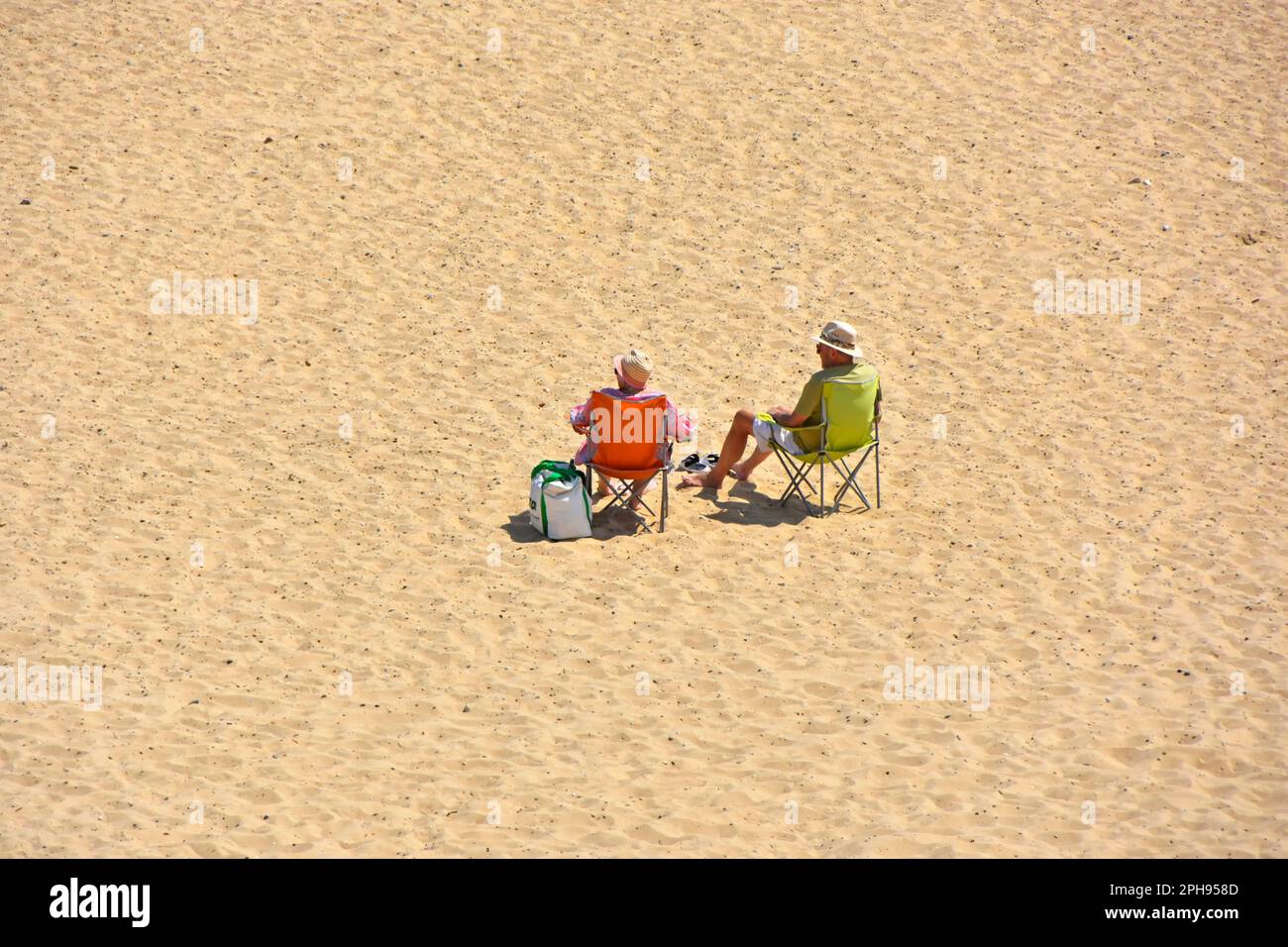 Wir blickten auf ein älteres Paar, das allein in Liegen auf einer scheinbar abgelegenen, leeren Weite von sauberem Sand am Meer in Sonnenhütten saß, heißes, sonniges Wochenende in Großbritannien Stockfoto